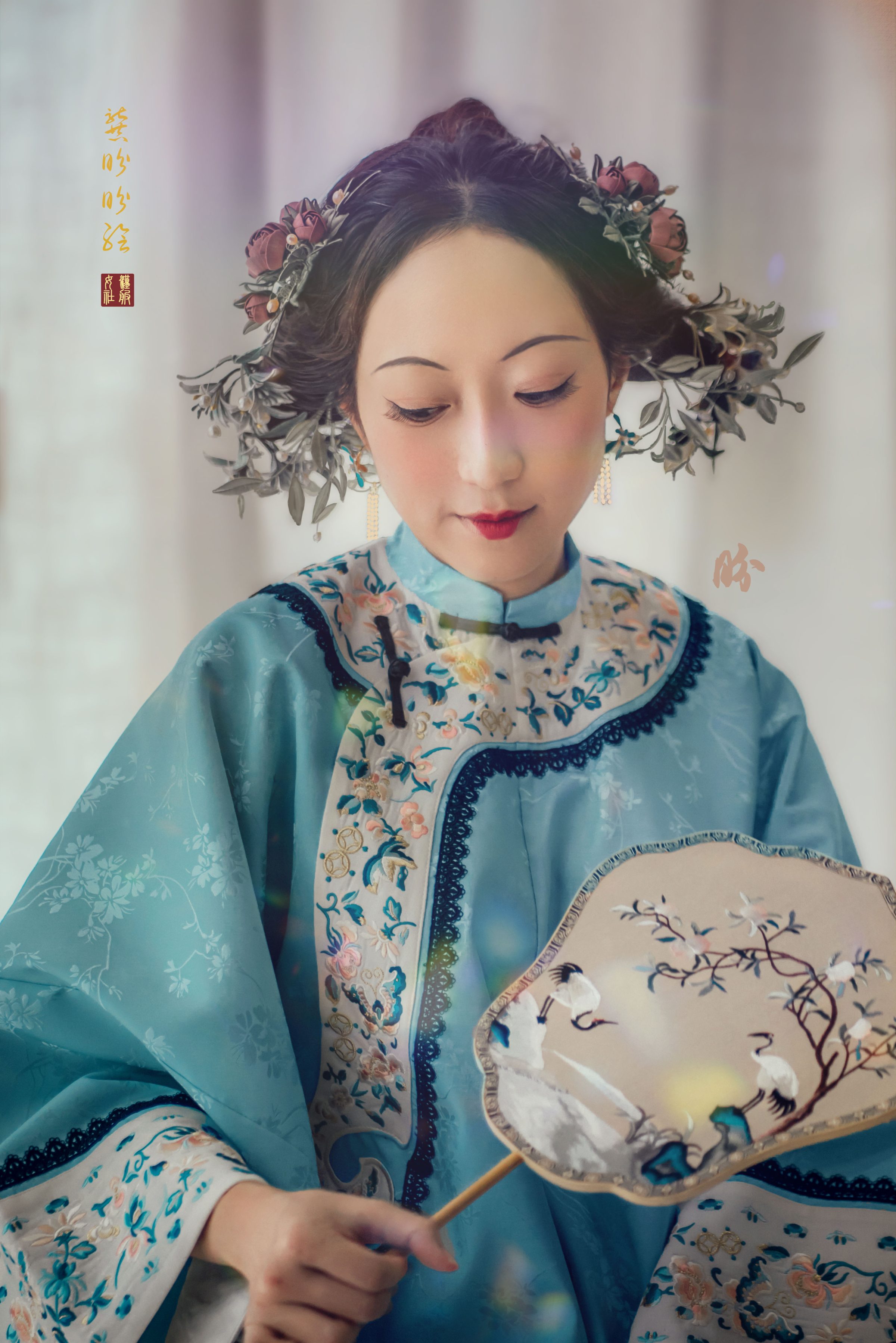 image of a Qing dynasty woman sometime in the late 19th century holding a fan embroidered with cranes, and a hair of wound silk flowers.